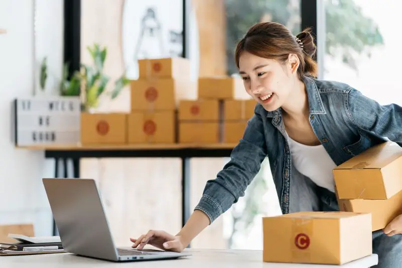 Asian woman entrepreneur is packing product to the box at home workplace.