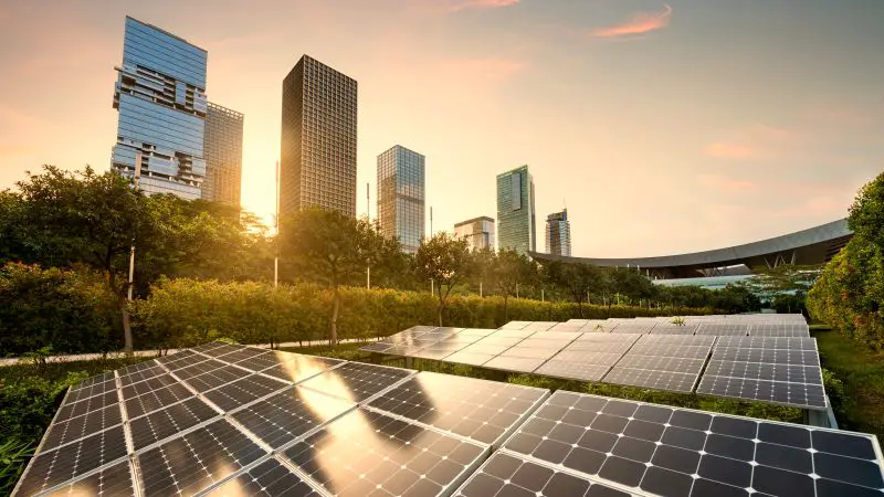Solar panels city landscape at sunset with buildings trees and bridge.