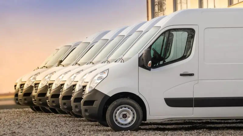 Row of white fleet vans parked in a lot.