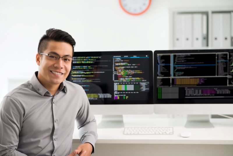 Young tech professional coding at dual monitors, symbolizing new talent from alternative education pathways.