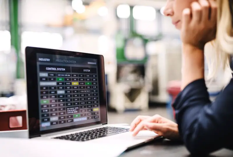 Employee reviewing real-time production system data on a laptop in an industrial workspace.