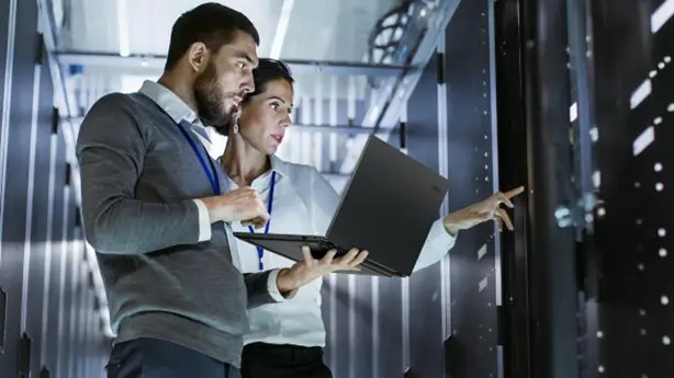 Two IT professionals working with a laptop in a data center.