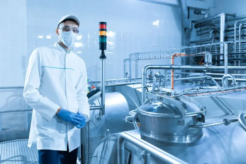 Inspector in a mask and a scrub stands with a folder-tablet in his hands at the dairy plant