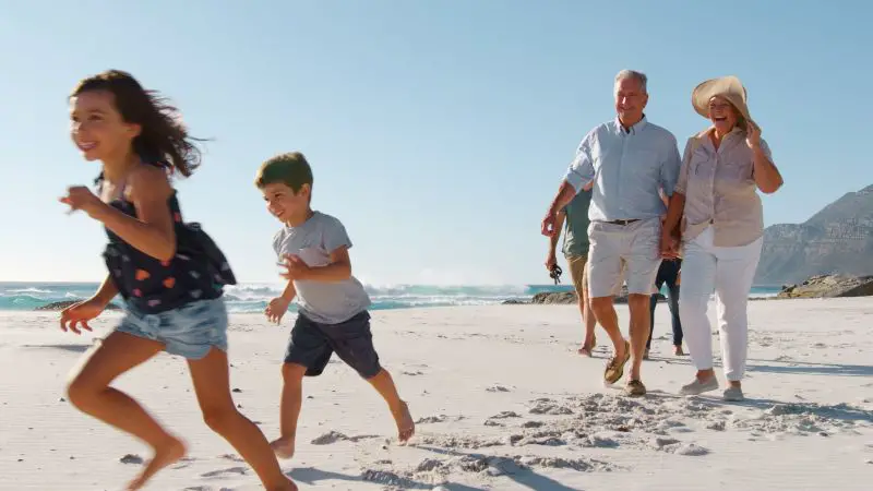 Multi Generation Family Meeting As They Walk Along Sandy Beach On Summer Vacation