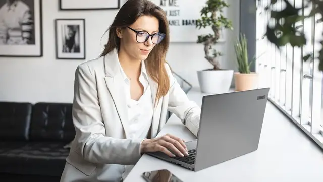 A businesswoman wearing eyeglasses, using a laptop.