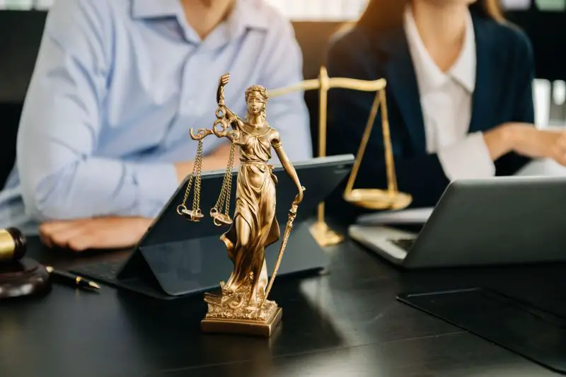 Business and lawyers discussing contract papers with brass scale on desk in office.