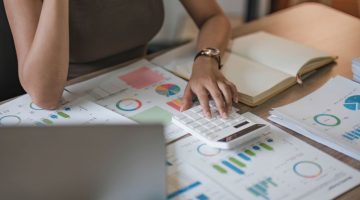 Close up of business woman using calculator and laptop for cash flow and finance calculations on wooden desk in office
