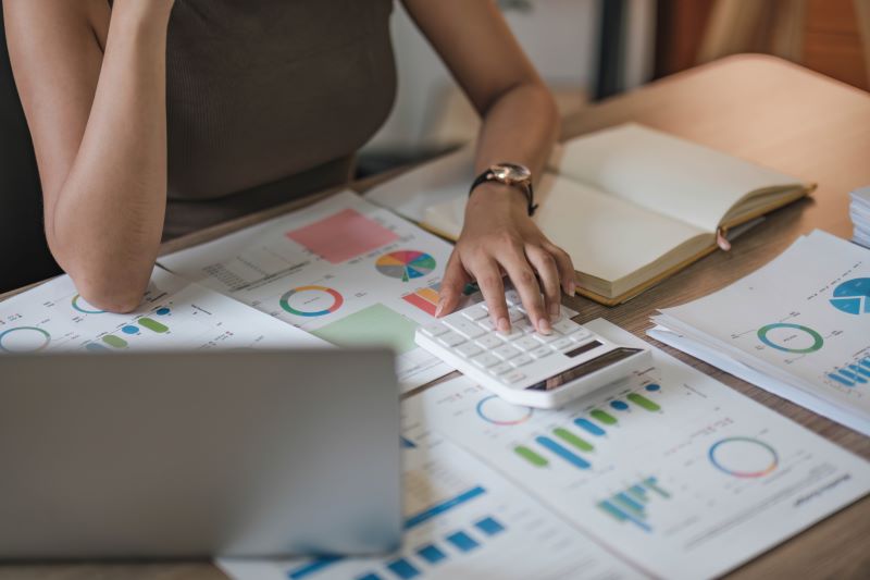 Close up of business woman using calculator and laptop for cash flow and finance calculations on wooden desk in office
