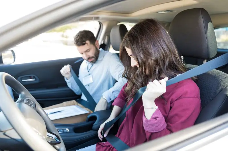Brunette Woman And Trainer Wearing Car Seatbelts