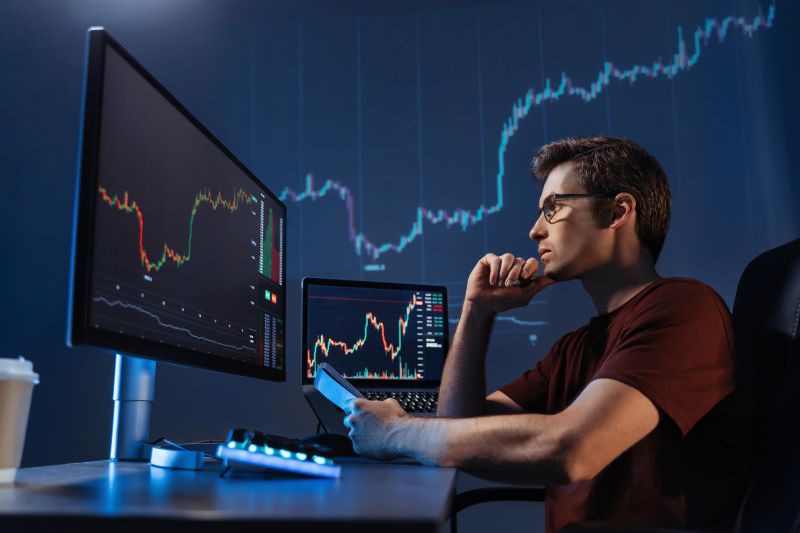 Crypto trader sitting in front of computers, making professional analysis of candlestick chart