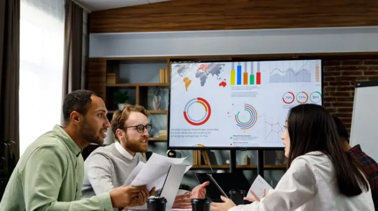 A team of young, mixed-race businesspeople is assessing the business metrics for the business retention strategy and audit.