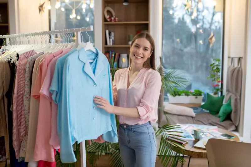 Young woman consultant showing women clothes presented in her showroom.