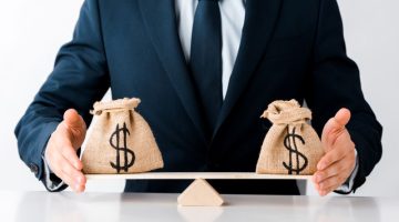 cropped view of businessman touching scales with money bags isolated on white