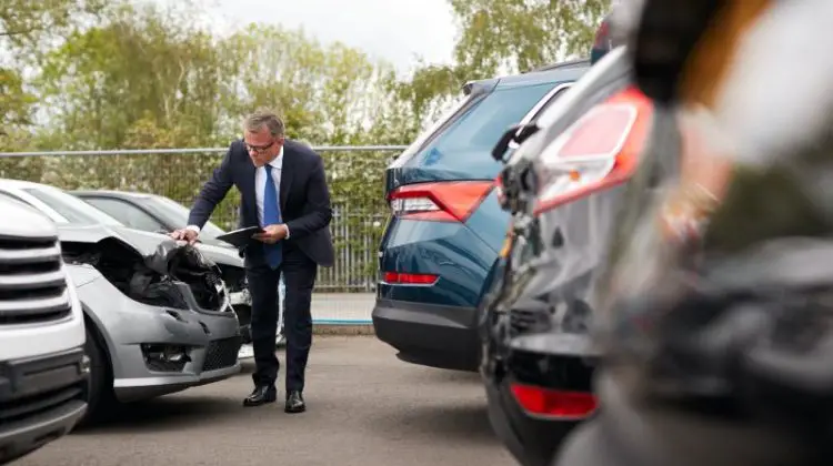 Male Insurance Loss Adjuster With Digital Tablet Inspecting Damage To Car From Motor Accident