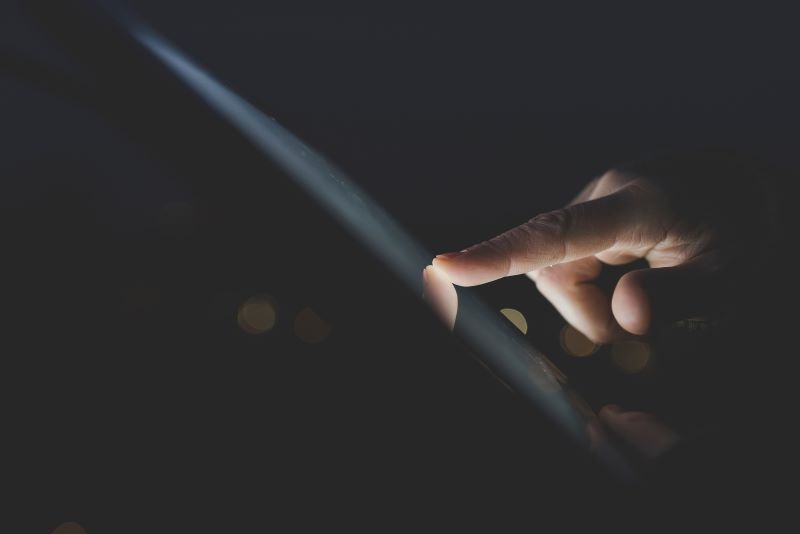 Close up of woman's finger using digital tablet touchscreen in darkness