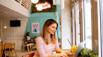 Young woman working on laptop and drinking fresh orange juice in the cafe