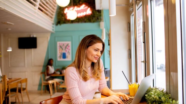 Young woman working on laptop and drinking fresh orange juice in the cafe