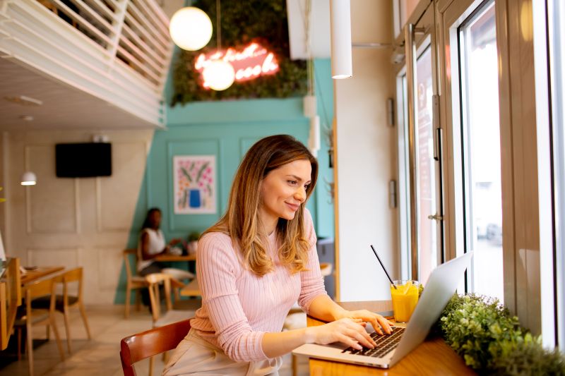 Young woman working on laptop and drinking fresh orange juice in the cafe