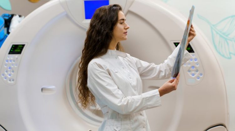 Young medical student in gown checks medical results post-CT scan in clinic.