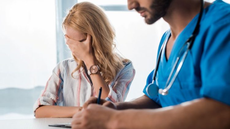 selective focus of woman covering face near doctor writing prescription