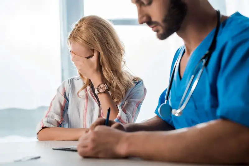 selective focus of woman covering face near doctor writing prescription