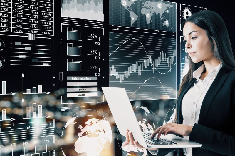 Attractive Young Businesswoman Using Laptop With Abstract Digital Business Interface in the Background