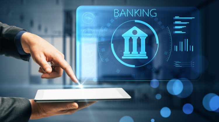 Businessman Hand Pointing At Tablet With Creative Online Banking Hologram On Blue Blurry