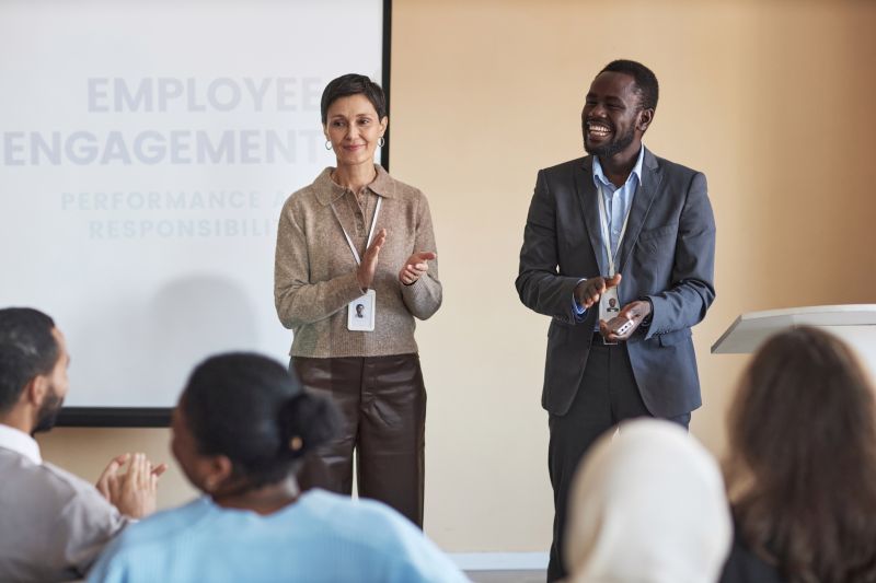 Successful mature coach and her assistant clapping hands in front of audience