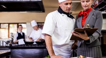 Female manager and male chef writing on clipboard in kitchen