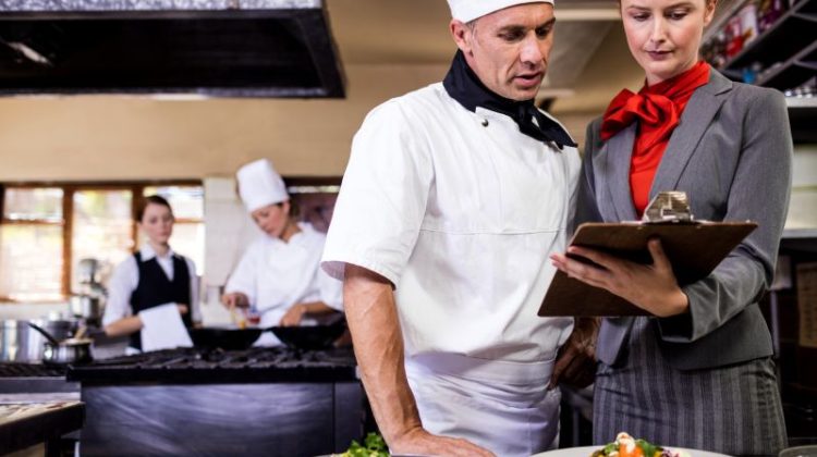 Female manager and male chef writing on clipboard in kitchen