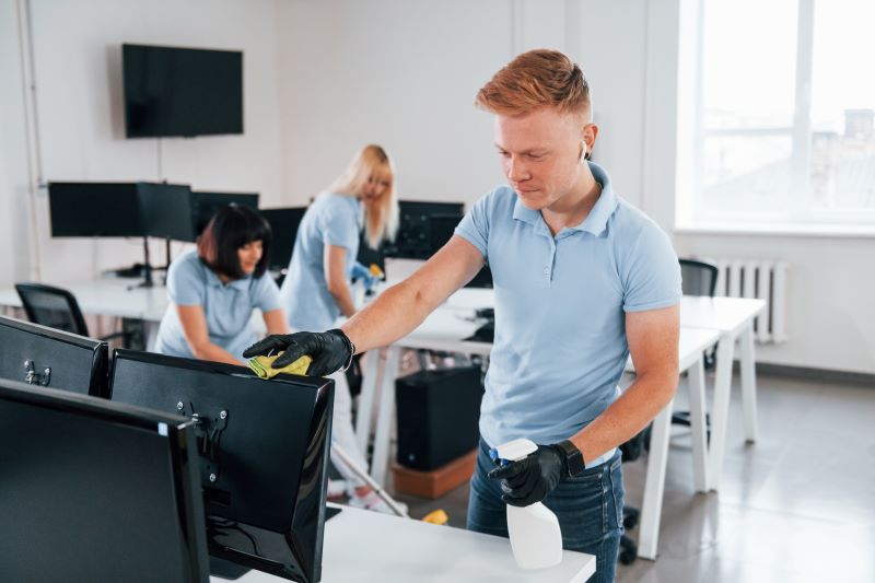 Cleans monitor. Group of workers clean modern office together at daytime