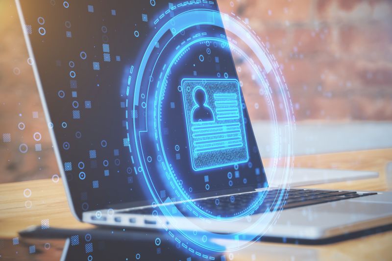 Close Up Of Desktop With Laptop And Abstract Glowing Digital Profile On Blurry Office Background