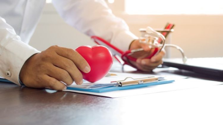 close up hand of doctor hold heart shape and checking on paper