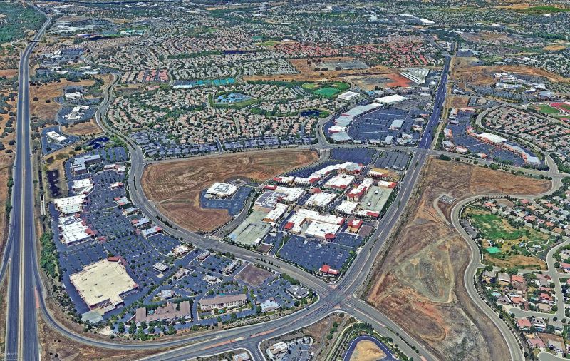 Close-up of shallow, muddy water with green plant stems emerging from the surface, possibly in a wetland or flooded area, partially obscured by a blurred foreground.