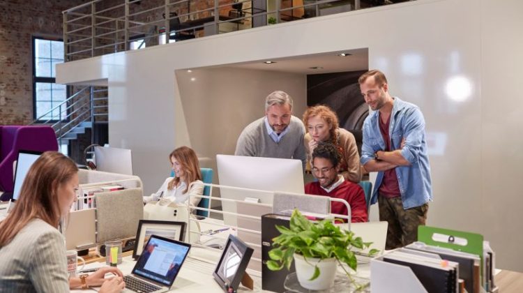Colleagues looking over shoulder of young man working in modern office