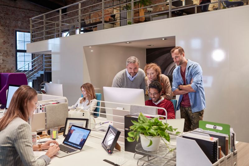 Colleagues looking over shoulder of young man working in modern office