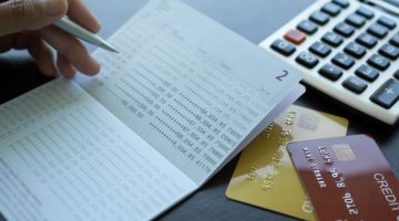 Finger holding pen poin number on book bank with caculator credit card