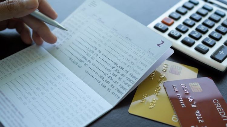 Finger holding pen poin number on book bank with caculator credit card