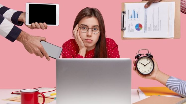 Brunette woman sitting at desk surrounded with gadgets and papers