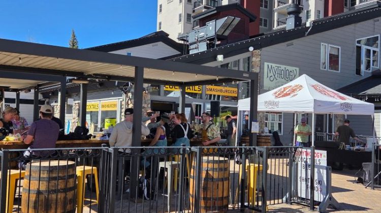A lively outdoor seating area at Mythology Distillery, Steamboat Springs, Colorado, where people are gathered around a bar counter and tables.