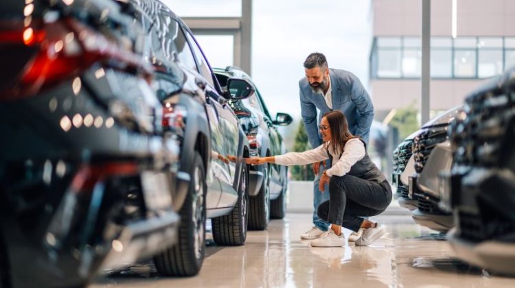 Woman and man examining cars on the showroom floor, discussing details
