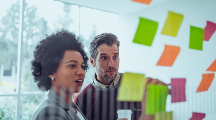 A man and woman stand together in a workplace collaborating on a project.