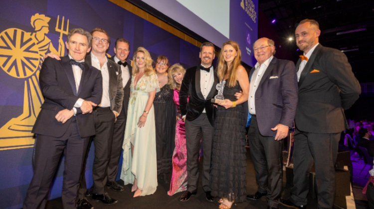 Champions Speakers team celebrate on stage at the British Business Awards after winning SME of the Year, holding their trophy alongside fellow attendees in formal evening wear