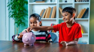 Indian Boy and Girl Siblings Putting Coins in Piggy Bank at Home – Saving and Learning Concept