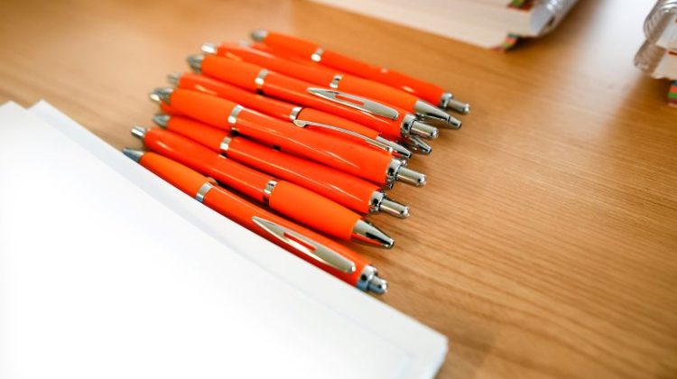 Stack of Orange Pens on Wooden Desk with Paper