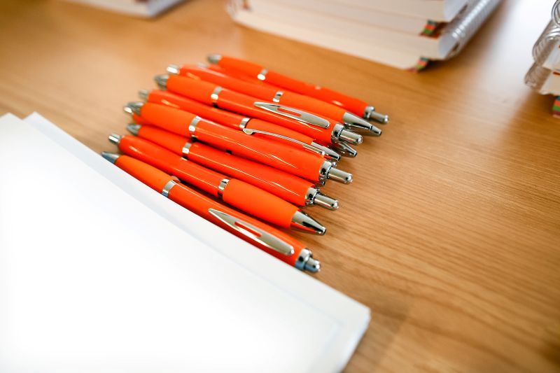 Stack of Orange Pens on Wooden Desk with Paper