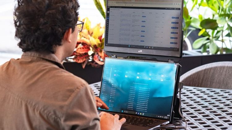 Remote professional using a portable dual-screen laptop monitor extension to multitask efficiently while working in a travel-friendly workspace.