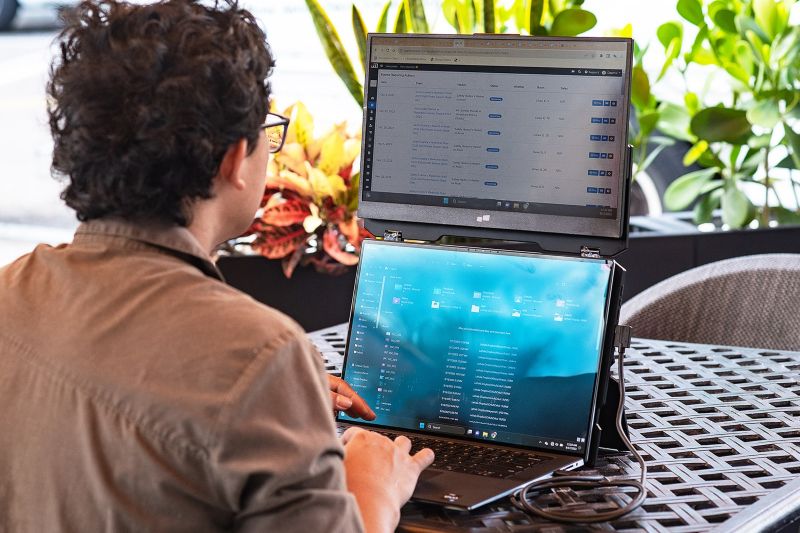 Remote professional using a portable dual-screen laptop monitor extension to multitask efficiently while working in a travel-friendly workspace.