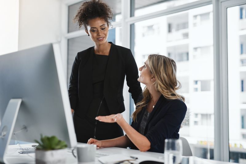 Two Women Discussing Project at Desk with Computer