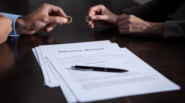partial view of couple at table with divorce documents holding rings